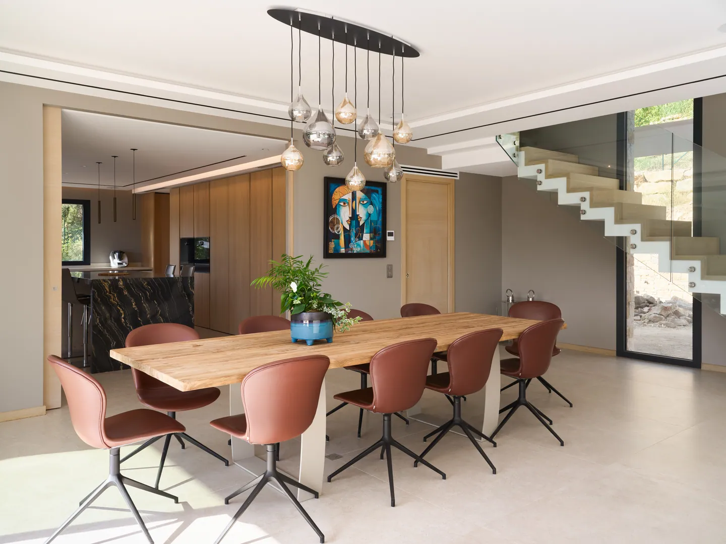 Salle à manger avec table en bois massif, chaises en cuir cognac et escalier suspendu