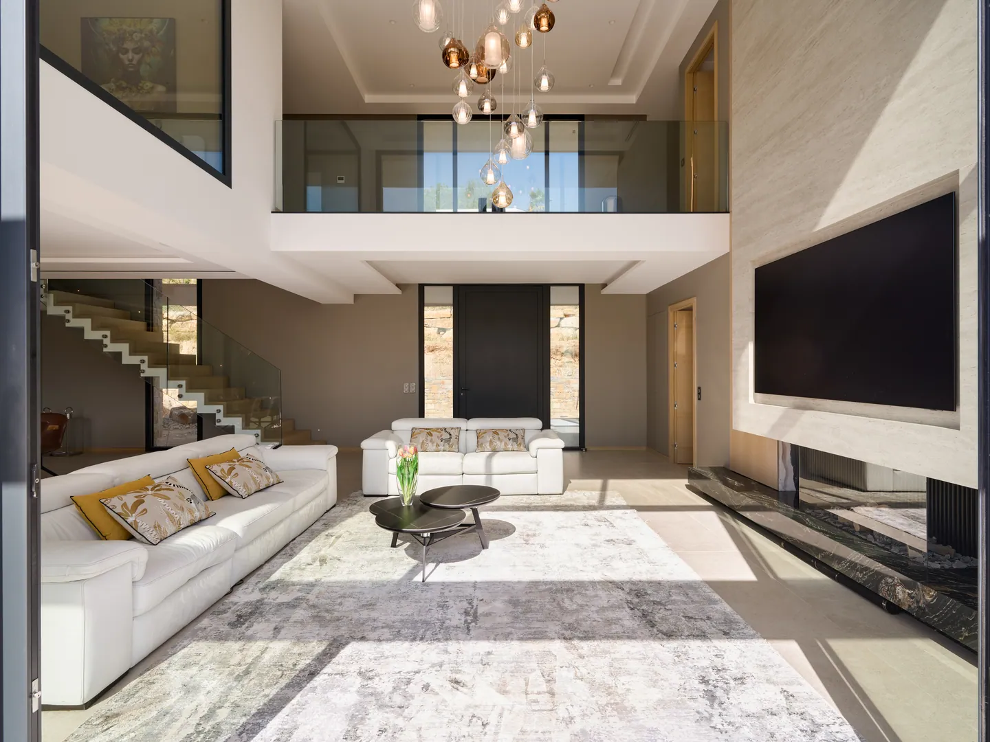 Volume double hauteur du séjour avec mezzanine vitrée, mur TV en pierre et canapés blancs