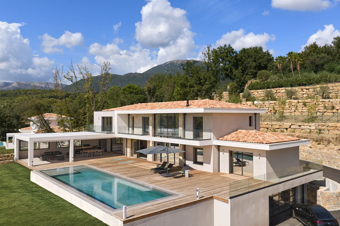 Villa contemporaine vue d'en haut avec piscine, grand deck en bois, pool house et montagnes en arrière-plan