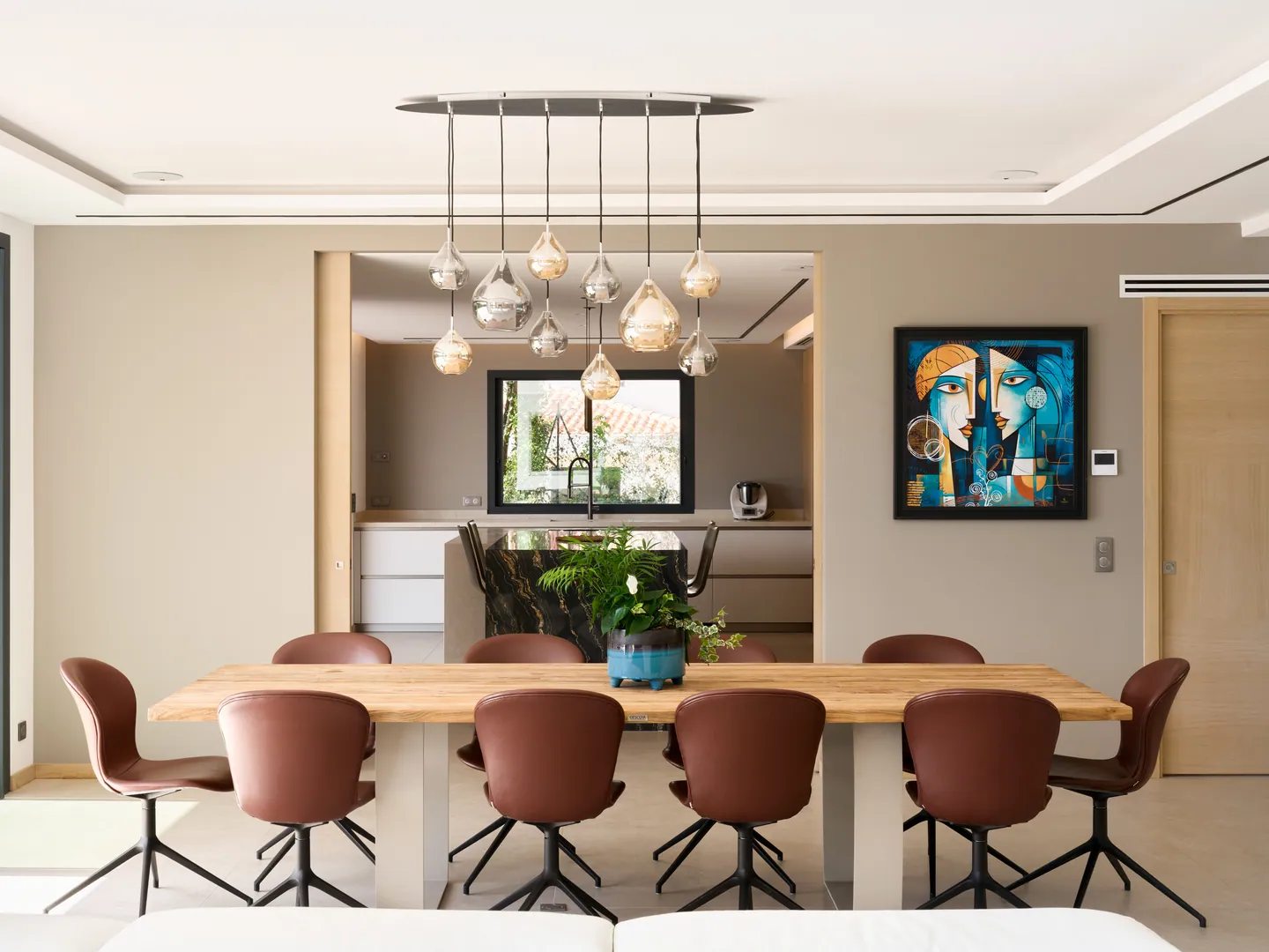 Longue table à manger en bois sous une suspension en verre, cuisine en arrière-plan