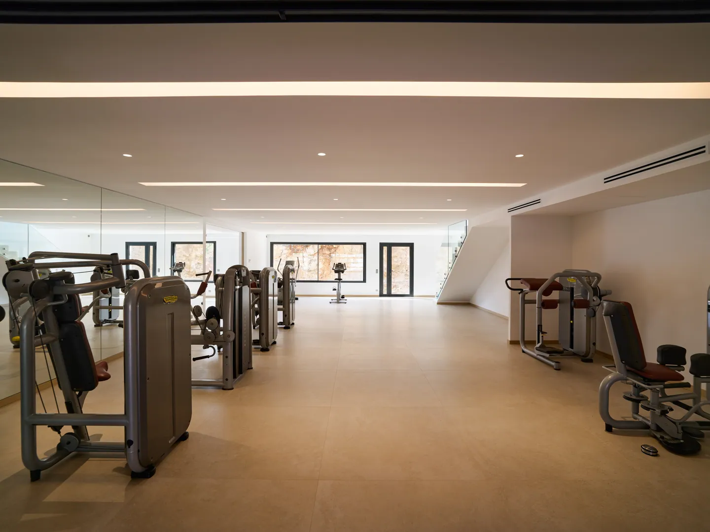 Salle de sport équipée de machines de musculation, mur de miroirs et éclairage linéaire