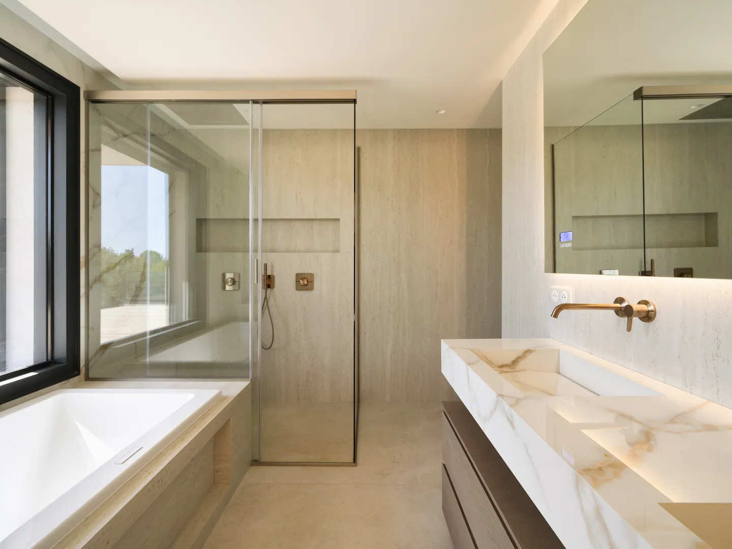 Salle de bains en pierre claire avec baignoire, douche vitrée et vasque en marbre rétroéclairée