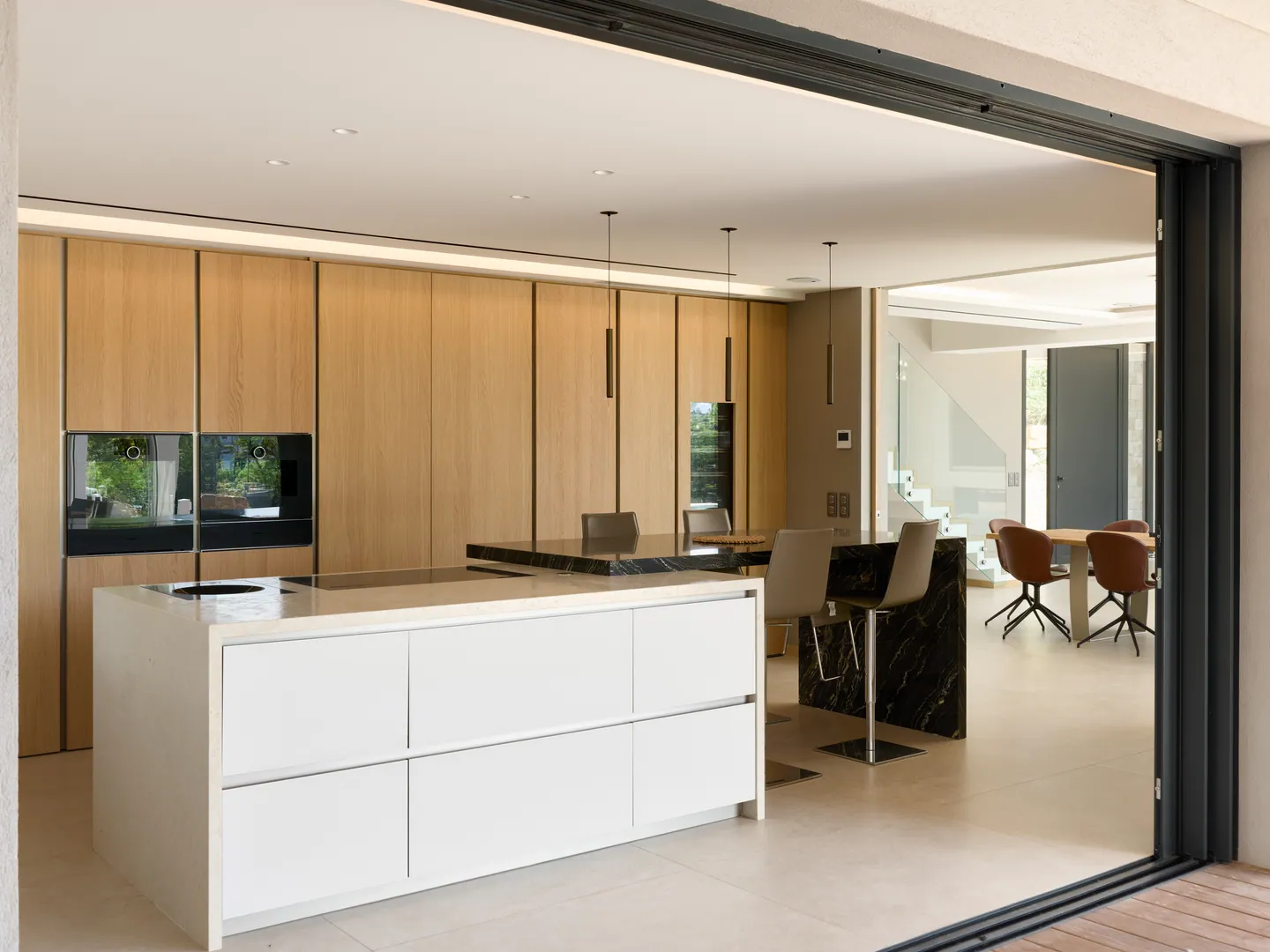Cuisine vue depuis la terrasse, îlot blanc et bar en marbre noir, salle à manger au fond
