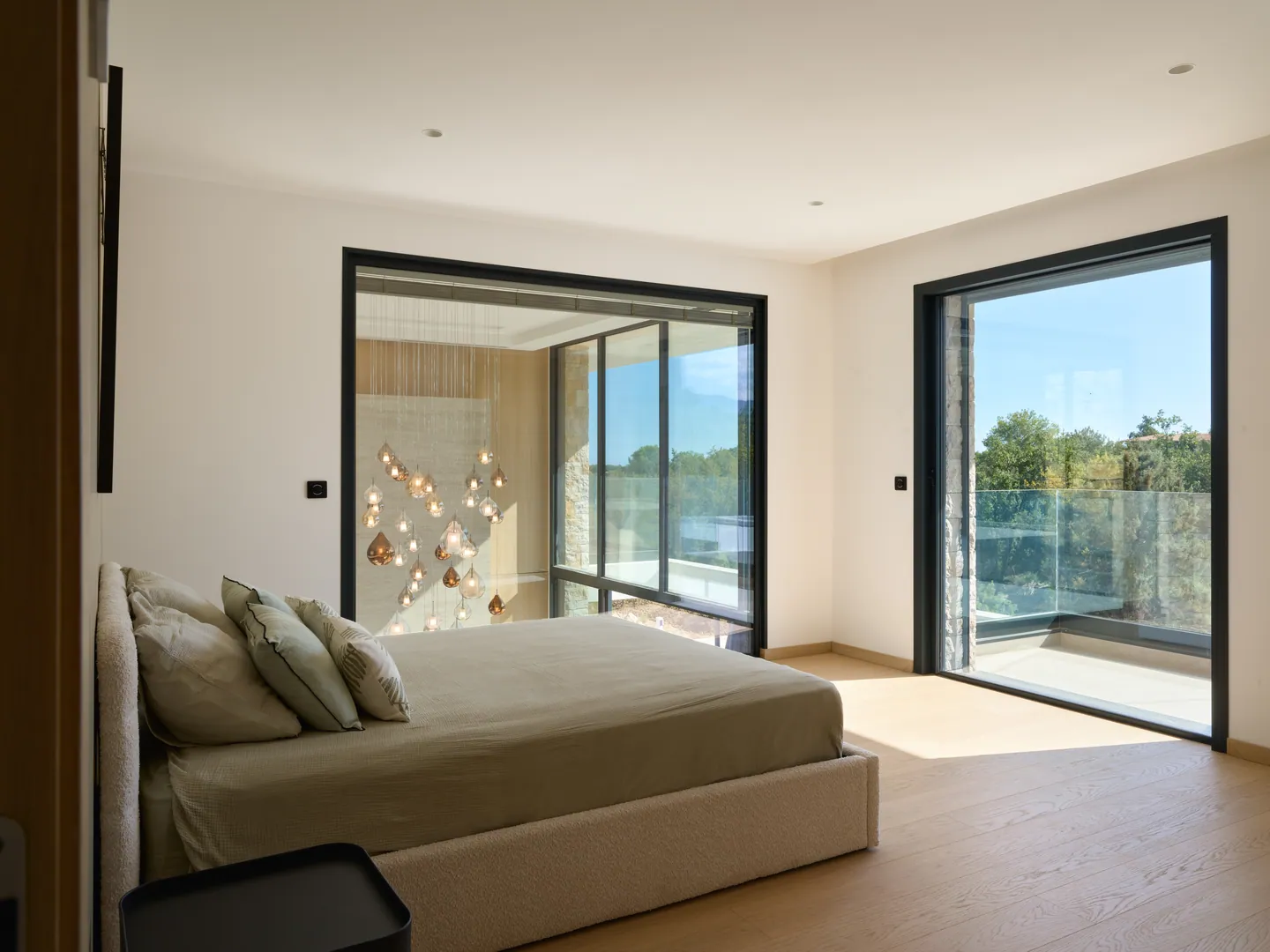 Chambre avec lit tapissé, baie sur le balcon vitré et fenêtre intérieure sur le lustre du séjour