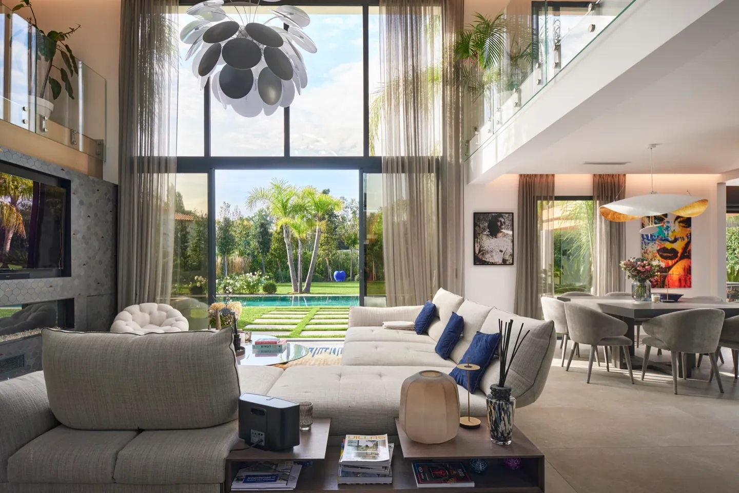 Double-height living room with sofas and dining area, glazing open to the garden and pool