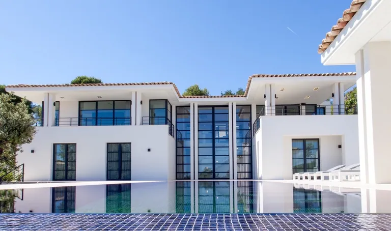 White villa with tiled roofs and tall black-framed glazing, pool in the foreground