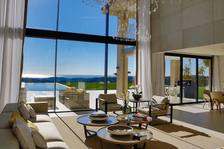 Double-height living room opening through glazing onto the infinity pool and the sea
