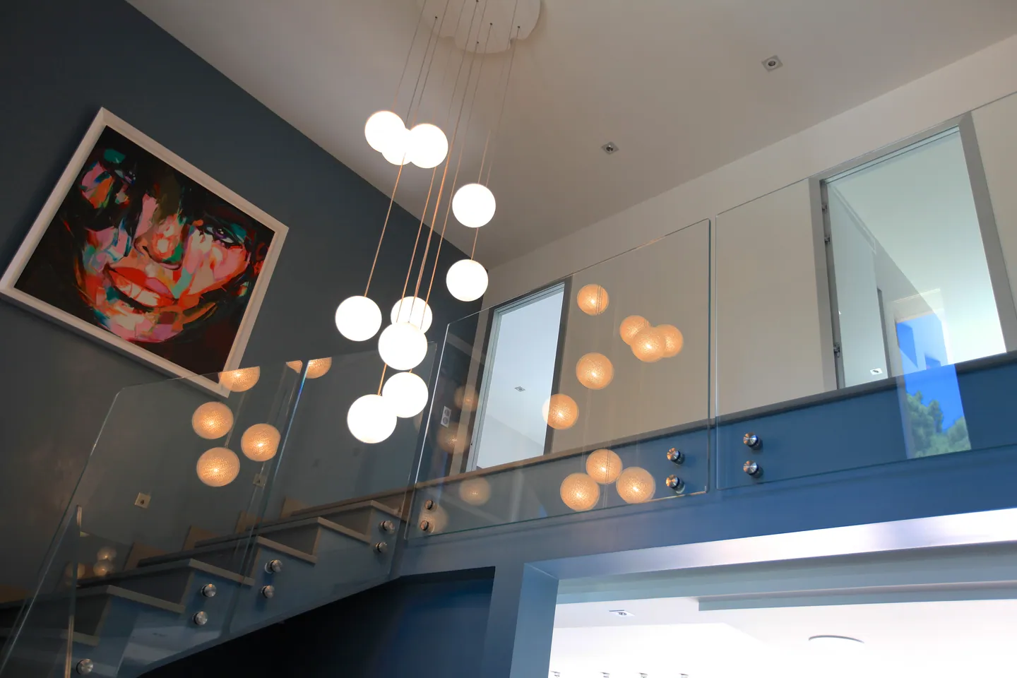 Escalier en verre sous une cascade de suspensions en globes, tableau coloré au mur